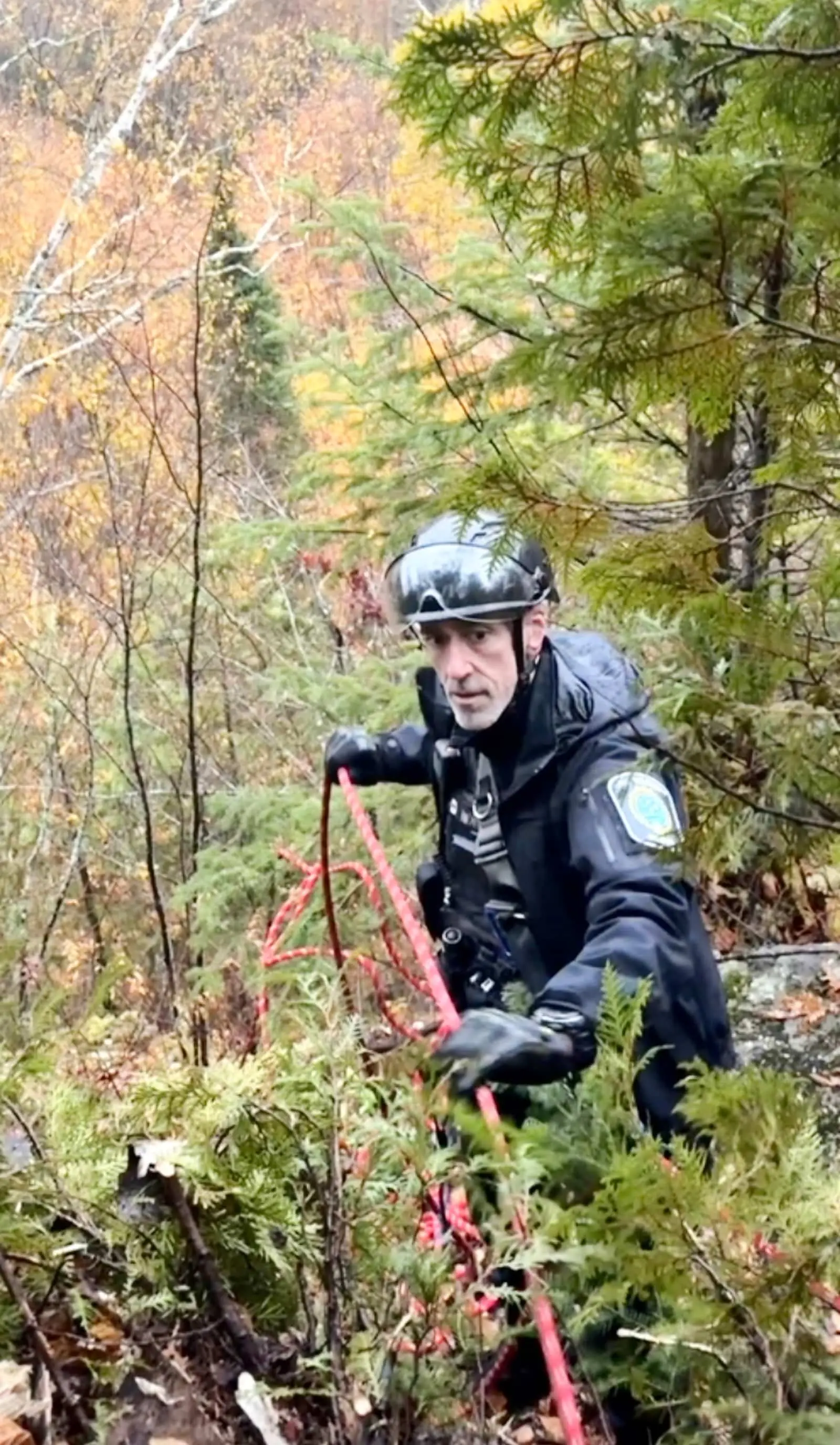 Steven Amorosa, casqué, tient une corde rouge à deux mains dans une pente boisée